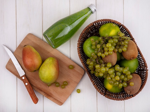 Pere di vista dall'alto con coltello sul tagliere con una bottiglia di succo di frutta e uva con mandarini nel cestello