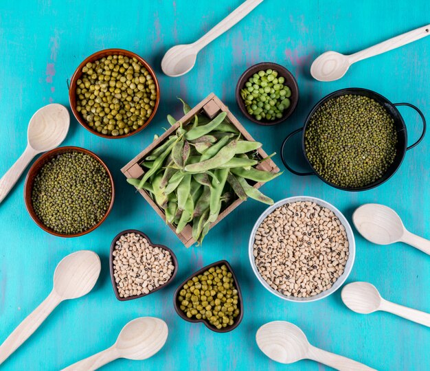 Top view of peas and beans in wooden box, bowls and spoons