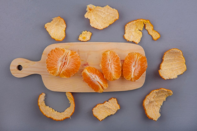 Top view peeled oranges on cutting board with peel on gray background
