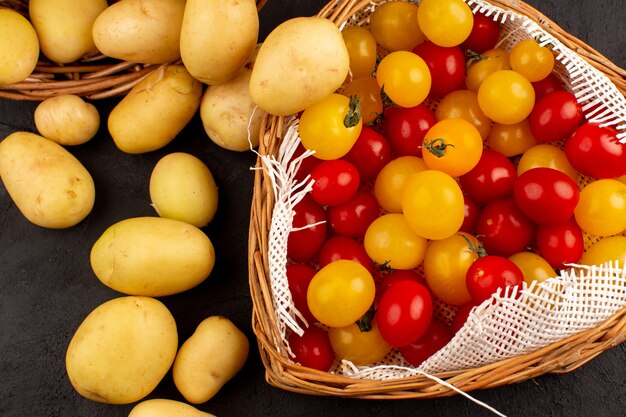 top view peeled out potatoes along with yellow and red tomatoes inside baskets on the grey floor