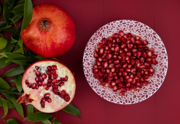 Top view of peeled pomegranate on a plate with leaf branches on a red surface