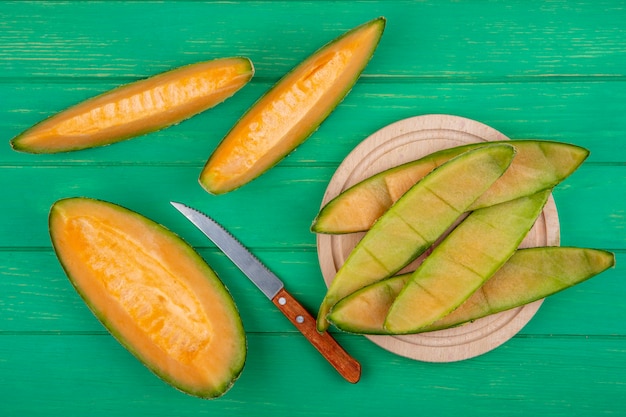 Top view of peels of melon on a wooden kitchen board with knife with slices of melon on green surface