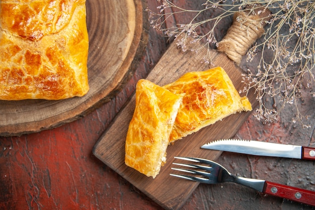 Top view of penovani khachapuri on wood board and on chopping board knife and fork on dark red surface