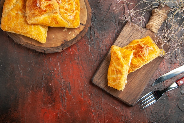 Top view of penovani khachapuri on wood board and on chopping board knife and fork on dark red surface