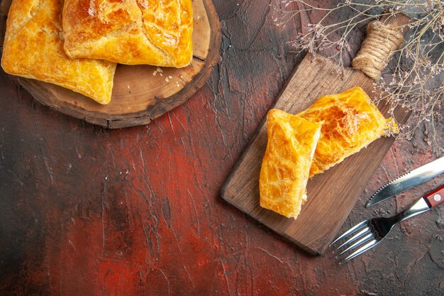 Top view of penovani khachapuri on wood board and on chopping board knife and fork on dark red surface