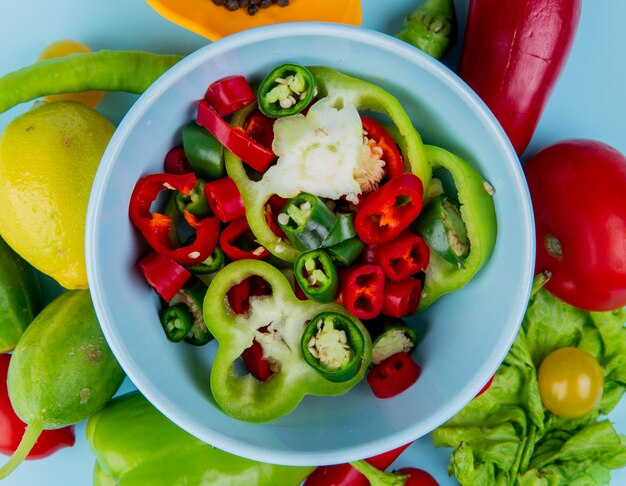 Top view of pepper slices in bowl with vegetables as tomato pepper lettuce with lemon on blue surface