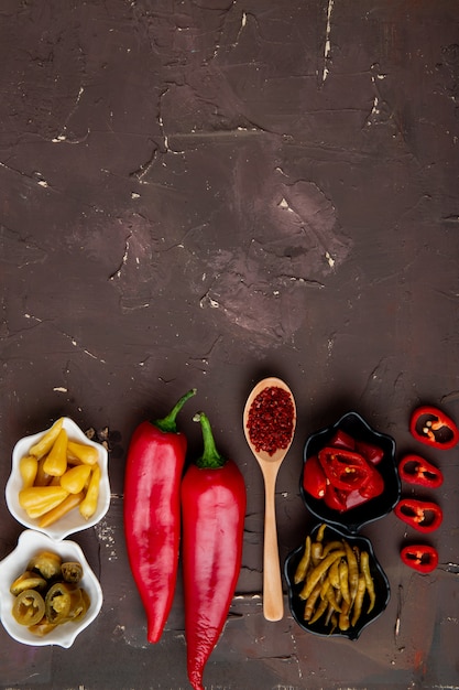 Top view of pepper and spoon of sumac with bowls of salted peppers on maroon background with copy space