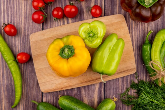 Top view of peppers on cutting board with dill tomatoes and cucumbers on wooden surface