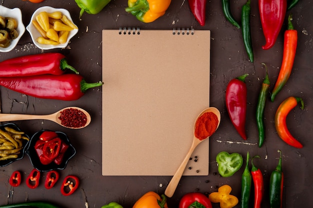 Top view of peppers and spices and salted peppers with note pad on maroon background with copy space