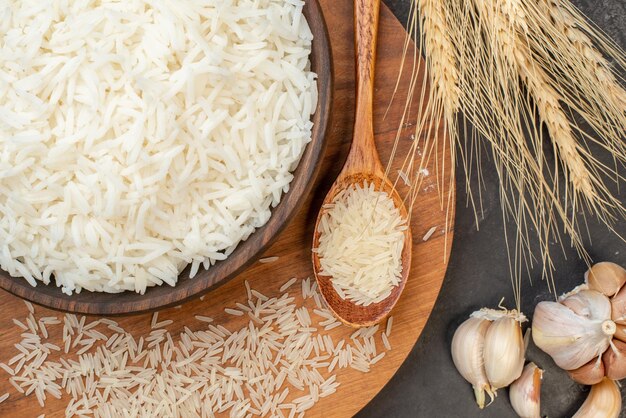 Top view of perfect long rice in brown pot and on wooden board garlics spike spoon on gray background