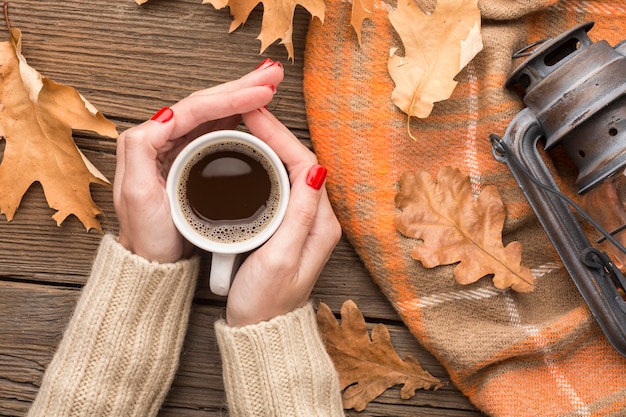 top view of person holding coffee cup with autumn leaves and lantern