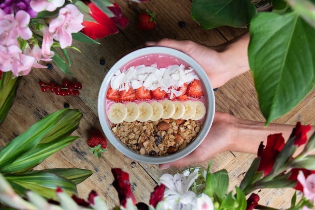 Top view of a person holding a healthy smoothie bowl with fruits and granola