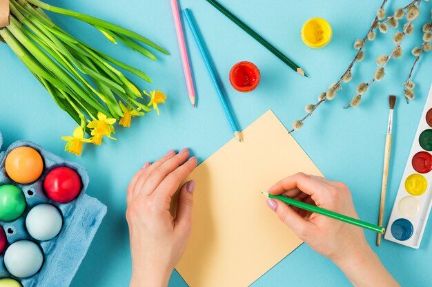 Top view of person painting Easter eggs and writing greeting card