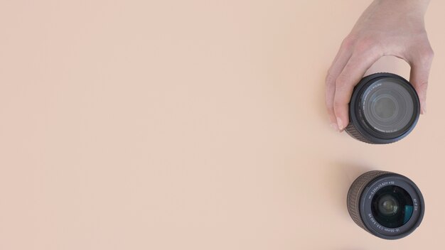 Top view of person's hand holding modern camera lens on beige background