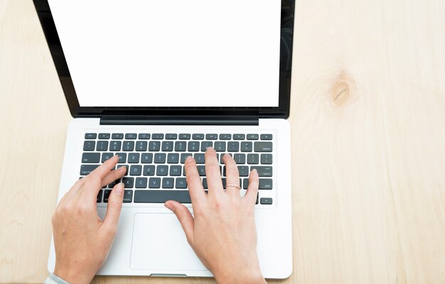 木製の背景の上にノートパソコンで入力している人の手の上の眺め