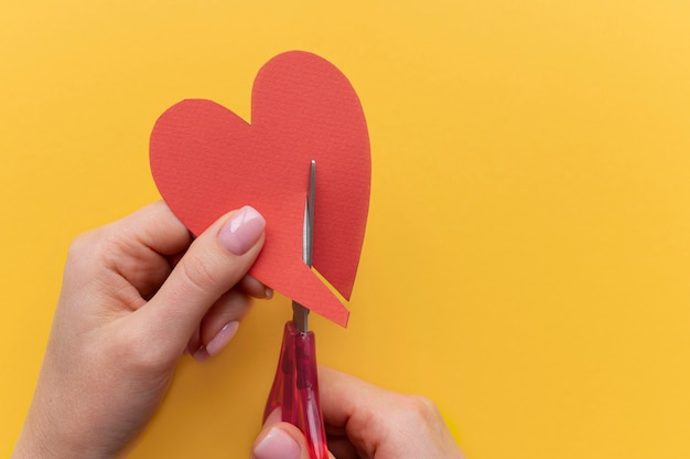 Free photo top view of person using scissors to cut a broken heart from paper