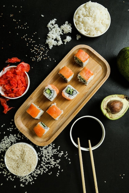 Free photo top view philadelphia rolls on a stand with ginger soy sauce avacado boiled rice and sesame seeds on a black table