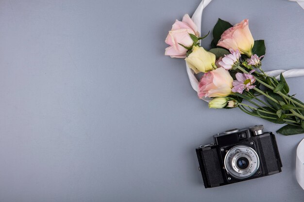 Top view of photo camera and flowers with ribbon on gray background with copy space