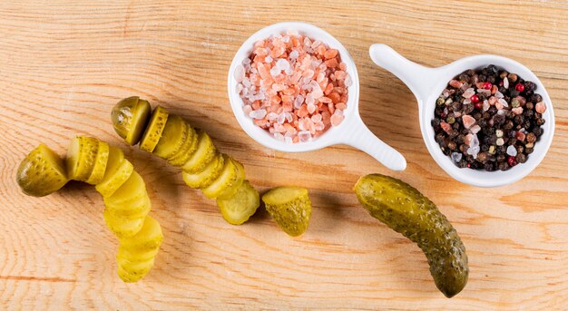 Top view pickled cucumber sliced with spices in bowls on biege wooden  horizontal