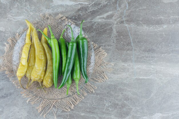 Top view of pickled and fresh green hot peppers on glass plate.