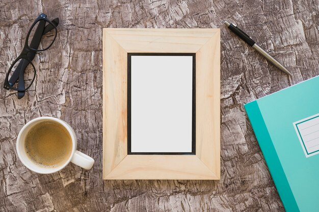 Top view of picture frame; coffee cup; eyeglasses; pen and notebook on textured background