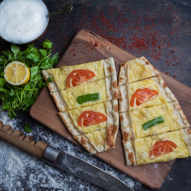 Top view pide with cheese and parsley and lemon and ayran in cutting board