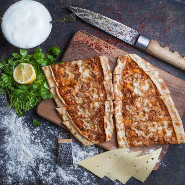 Top view pide with minced meat and cheese and ayran and knife in cutting board