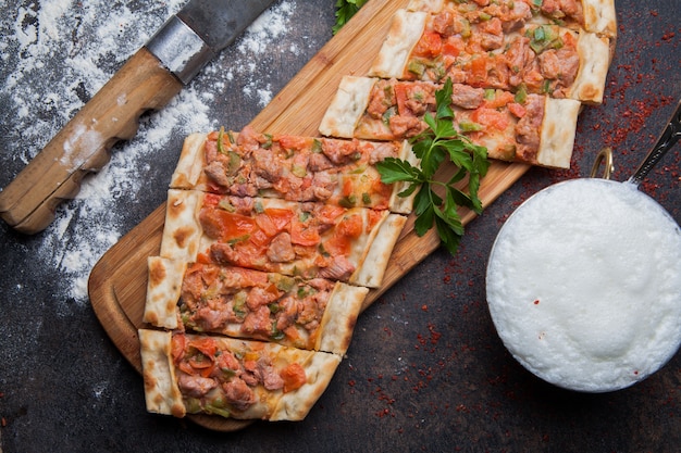 Top view pide with pieces of meat and knife and ayran in cutting board