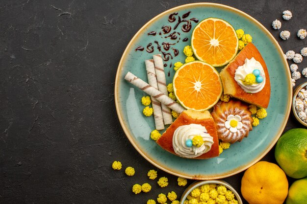 Top view pie slices with sliced fresh tangerines and candies on dark desk