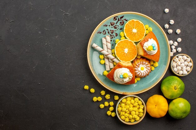 Top view pie slices with sliced fresh tangerines and candies on dark