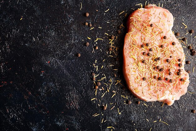 Top view on piece of raw steak meat seasoned with pepper, salt and dry rosemary on dark wooden table