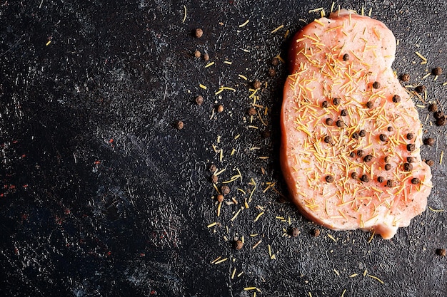 Top view on piece of raw steak meat seasoned with pepper, salt and dry rosemary on dark wooden table