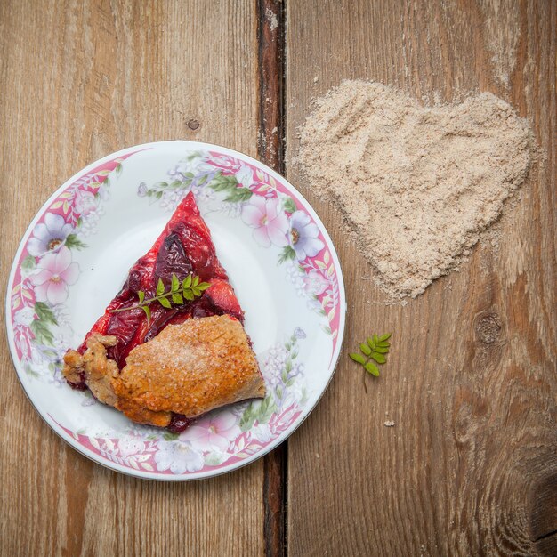Top view piece of strawberry pie with nut crumbs and heart in round flower plate