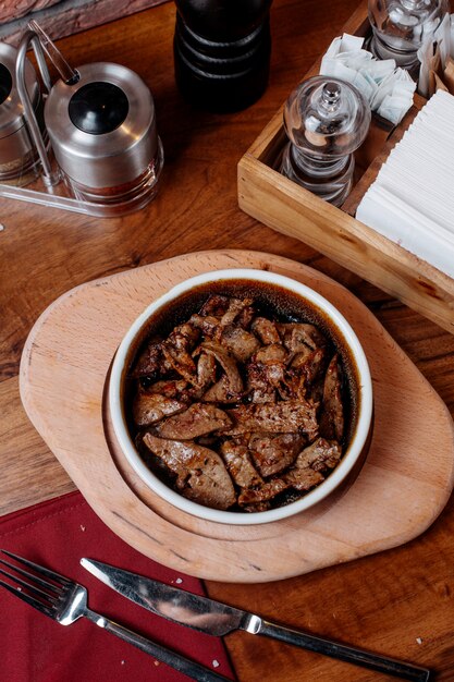 Top view of pieces of beef fried in a clay bowl with spices on a wooden board