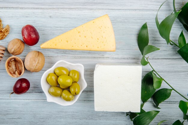 Top view of pieces of cheese with fresh grape, pickled olives and walnuts on grey wooden table