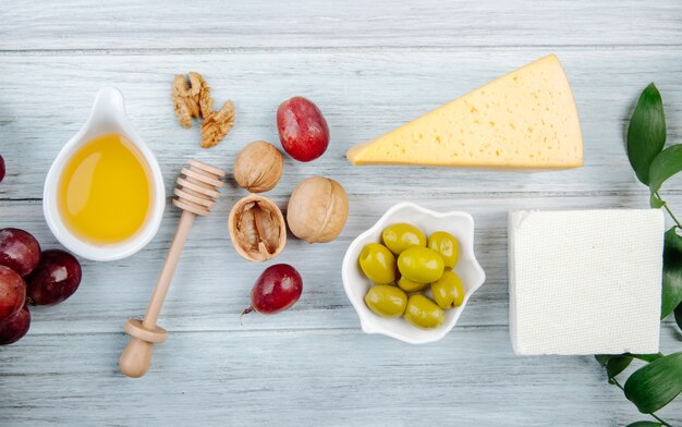 Top view of pieces of cheese with honey, fresh grape, pickled olives and walnuts on grey wooden table