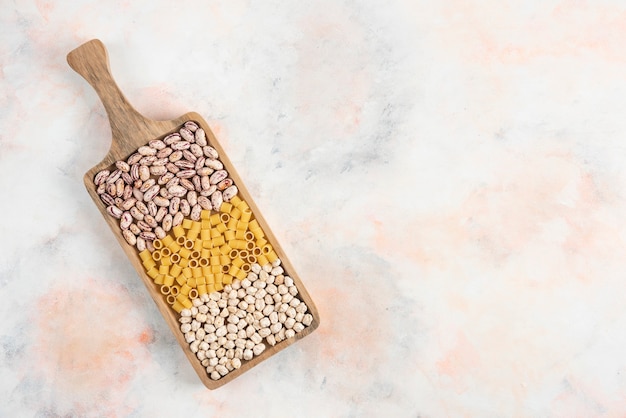 Free photo top view of pile of bean, pasta and chickpea on wooden tray.