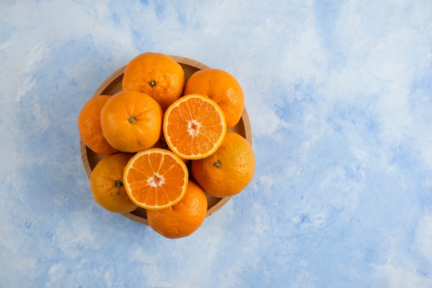 Top view. Pile of clementine mandarins on wooden plate over blue surface