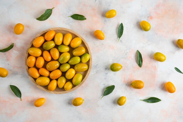 Top view of pile of kumquats on wooden plate over colorful surface