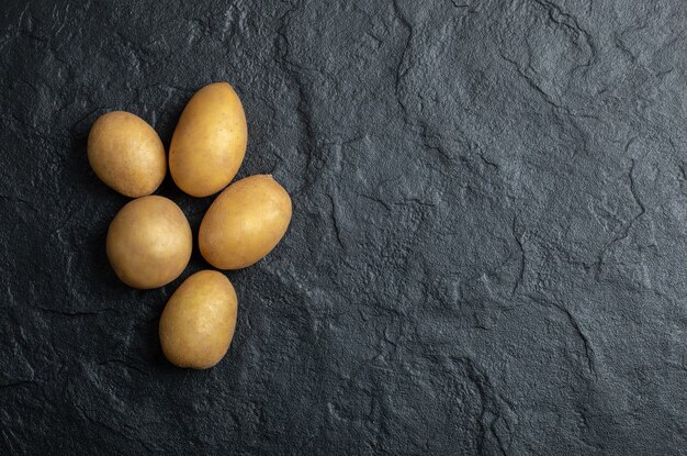 Top view of pile of potatoes. Fresh potatoes on black stone background. 