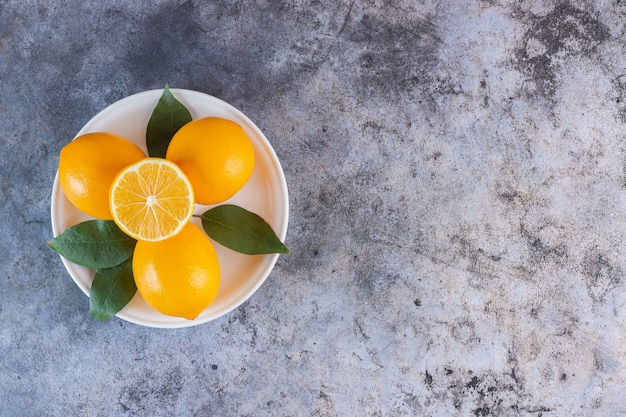 Вид сверху на кучу спелых лимонов на белой тарелке над серым.