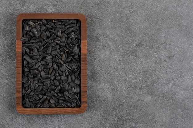 Top view. Pile of sunflower seeds in wooden bowl over grey surface. 