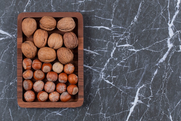 Top view. Pile of walnut and Hazelnut on wooden plate over black.