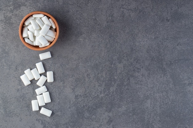 Top view of pile of white gums in wooden bowl over grey background.