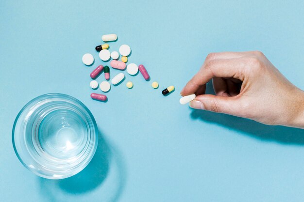 Top view of pills with glass of water and hand