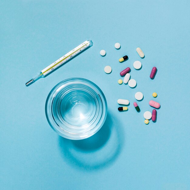 Top view of pills with thermometer and glass of water