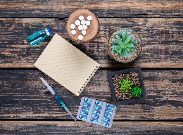 Top view pills on wood stub with cactus, notepad and needle on dark wooden background.