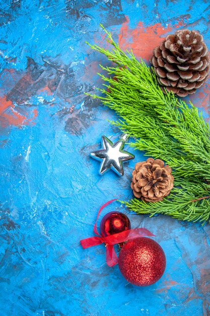파란색-빨간색 표면에 솔방울과 화려한 크리스마스 트리 장난감이 있는 상위 뷰 소나무 가지