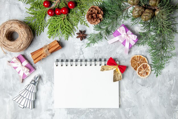 Top view pine tree branches notebook straw thread cinnamon sticks small gifts on grey background