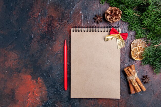 Top view pine tree branches and pinecones a notebook red pen anises cinnamon on dark red surface free space